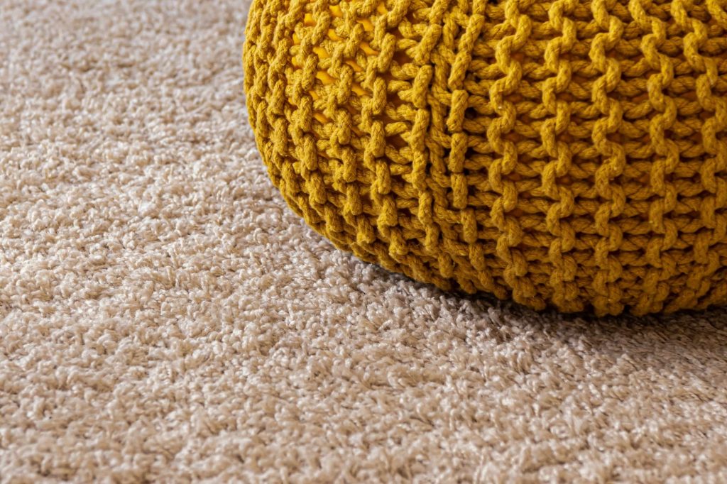 A close up of a cream coloured carpet remnant with a yellow, knitted plushie sat on top of it